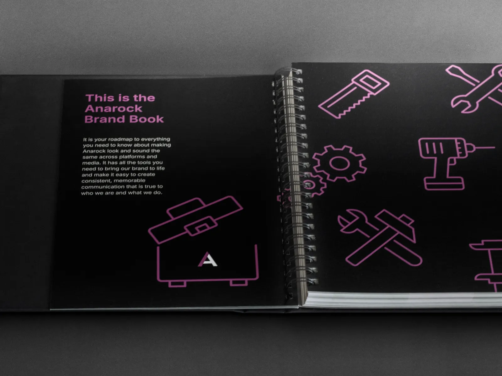 Open Anarock brand book spread titled 'This is the Anarock Brand Book' with pink line-art tool icons