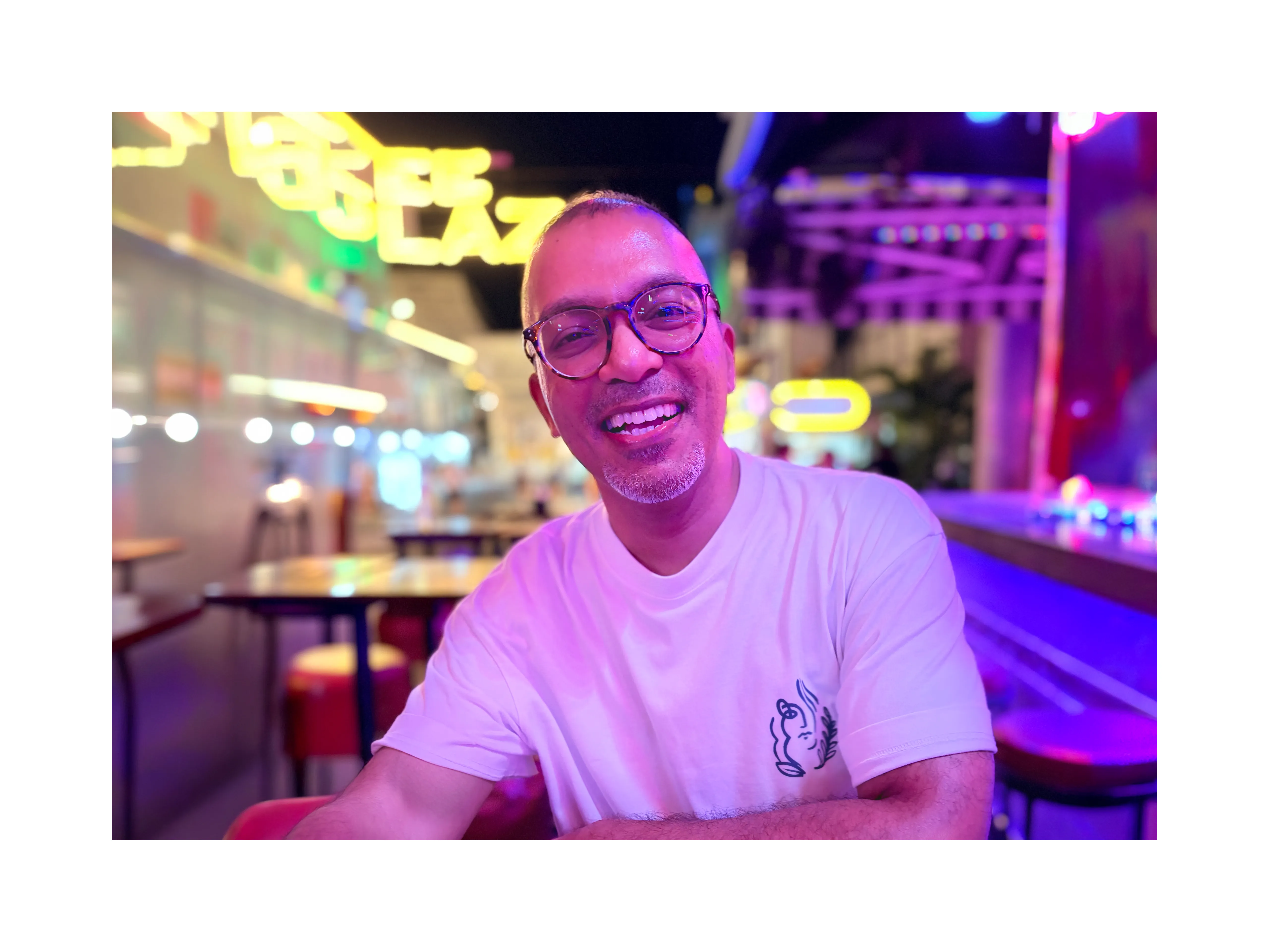 Geo George smiling, seated in a neon-lit arcade venue